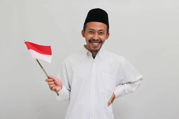 8月17日 一名身穿红衣 山核桃或Kopiah的兴奋的印度尼西亚年轻人举着一面印度尼西亚小旗庆祝印度尼西亚独立日 这面旗帜是白色背景的 — 图库照片