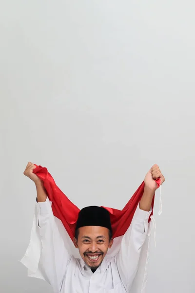 8月17日是印度尼西亚独立日 一名身穿歌袍 胸衣或Kopiah的兴奋的印度尼西亚年轻人举着一面印度尼西亚国旗庆祝印度尼西亚独立日 印尼独立纪念日是在白人背景下被隔离的 — 图库照片