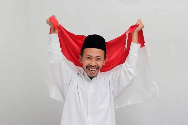 8月17日にインドネシア独立記念日を祝うためにインドネシアの国旗を掲げ 白い背景で孤立した 興奮する若いインドネシア人男性 — ストック写真