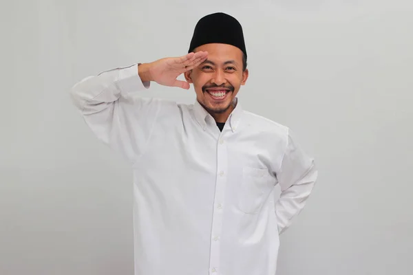 ワクワクする若いインドネシア人男性は ソングコック ピッチ またはコピアを着て 8月17日にインドネシアの独立記念日を祝いながら 白い背景で孤立したカメラに敬意を表しています — ストック写真