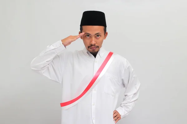 エキサイティングな若いインドネシア人男性は 赤と白のサッシを身に着け ピシアかピシアのいずれかを着て 8月17日にインドネシアの独立記念日を祝いながら敬意を表しています — ストック写真