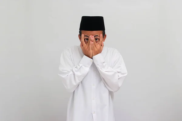 スカーレッド ヤング インドネシア人男性は ソングコック ピッチ またはコピアを着て 彼の顔を手のひらで覆い 白い背景に隔離された彼の指を覗いています — ストック写真