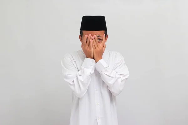 害怕的印度尼西亚年轻人 头戴头巾 胸针或Kopiah 用手掌捂住脸 用手指窥视 被白色背景隔开 — 图库照片
