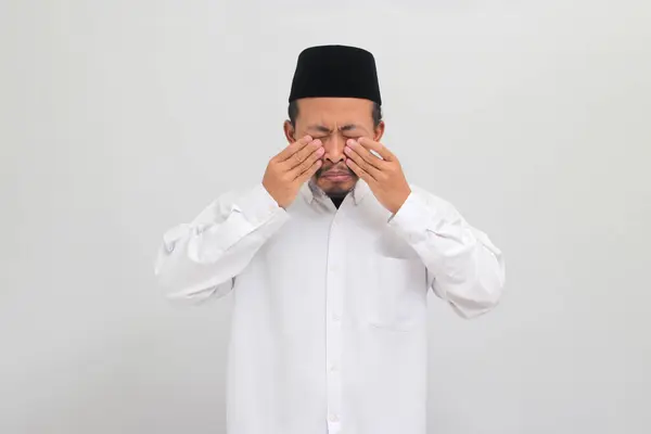 若いインドネシア人男性 ソングコックを着て Peci またはコピア 痛みの目を経験 ほこりのアレルギーとかゆみのために彼の腫れた目をこすり 白い背景に隔離 — ストック写真