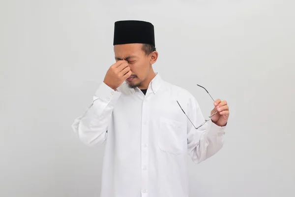 若いインドネシア人男性は ソングコック ピッチ またはコピアを着て 彼の鼻をピンチし 過労のためにめまいを感じ 白い背景で孤立しています — ストック写真