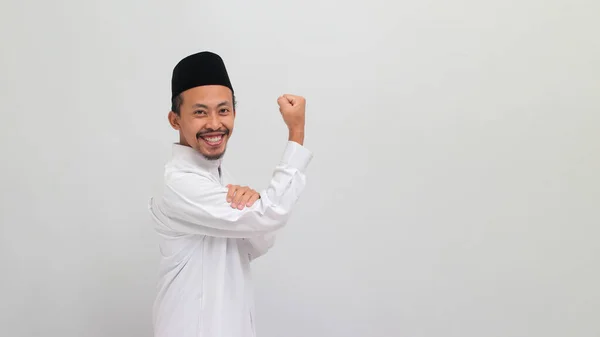 有自信的印度尼西亚年轻人 身穿歌颂 山核桃或Kopiah 做了一个强有力的手势 用手臂和肌肉对着摄像机 用白色背景隔离 表现出他的力量 — 图库照片