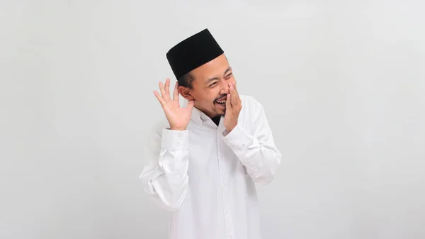 ワクワクする若いインドネシア人男性は ソングコック ピッチ またはコピアを着て 彼の耳の上に手を置き 白い背景に隔離された噂やゴシップを聞きながら微笑んでいます — ストック写真