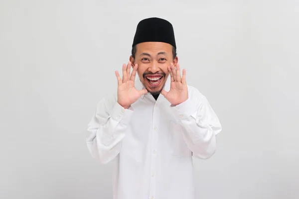 ワクワクする若いインドネシア人男性は ソングコック ピッチ またはコピアを着て 彼の口の近くに手を保ち 白い背景で孤立した秘密を囁いています — ストック写真