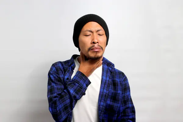Young Asian man in beanie hat and casual shirt is experiencing a sore throat, possibly due to irritation or an infection, Isolated on white background. Healthcare and medical concept.