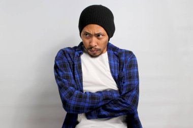 Kızgın, gücenmiş Asyalı genç bir adam kollarını kavuşturmuş, tatminsiz ya da hoşnutsuz bir tavır sergiliyor beyaz arka planda izole edilmiş boş fotokopi alanına bakarken..