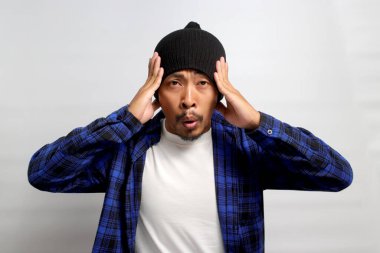 Gergin genç Asyalı adam sakinleşmek için adımlar atıyor, nefes alma tekniklerine odaklanıyor, muhtemelen baş ağrısını gideriyor ya da stresi yönetiyor, beyaz bir arka planda izole edilmiş.