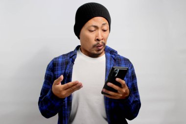 Şapkalı ve sıradan gömlekli sinirli Asyalı adam, kötü bir şey okurken küçümseyici tepki veriyor. Muhtemelen nahoş bir şaka ya da telefonundaki uygunsuz içerik beyaz arka plana yansıyor.