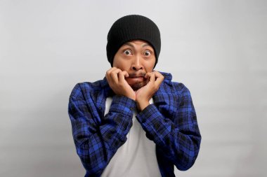 Utangaç genç Asyalı adam kameraya bakarken parmaklarını ısırıyor, şok, güvensizlik, endişe, hayal kırıklığı, kafa karışıklığı ve işle ilgili sorunlar hakkında korku gösteriyor..