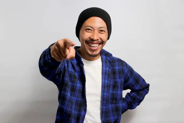 Its you. Young Asian man, dressed in a beanie hat and casual shirt, smiles while pointing his finger at the camera, choosing, inviting people, recruiting, standing over white background