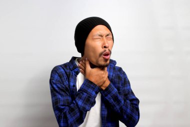 Genç Asyalı bir adam boğaz ağrısı çekiyor, rahatsız ve rahatsız, beyaz arka planda izole edilmiş. Öksürüyor ve elini boynunda tutuyor. Sağlık sigortası ve tıbbi konsept..