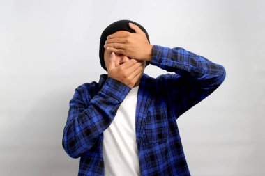 Şapka ve günlük tişört giyen üzgün Asyalı genç adam, ağlarken yüzünü kapatıyor. Hayattaki zorluklar, sorunlar ve duygusal zorluklarla boğuşuyor gibi görünüyor.