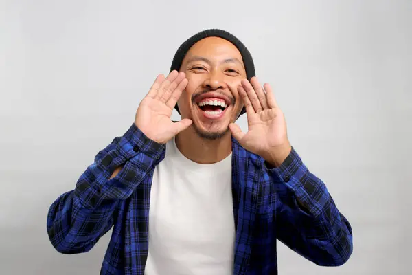 An excited young Asian man, dressed in casual clothes and wearing a beanie hat, is enthusiastically shouting to share some great news about a discount sale. Hurry up and take advantage of it