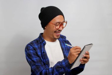 Gözlüklü, bereli ve günlük kıyafetleri olan çalışkan bir Asyalı öğrenci, elinde bir defter ve kalem tutarken not alırken yakalanır. Okumak, dil öğrenmek ve sınavlara hazırlanmak..