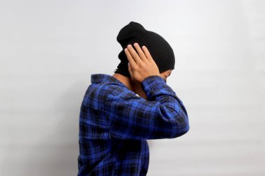 Sinirli Asyalı genç adamın yan görünüşü kulaklarını kapatıyor ve bağırıyor ya da bağırıyor gibi görünüyor. Kulak ağrısı, kulak iltihabından kaynaklanıyor olabilir.