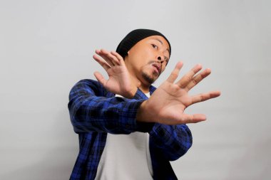 Iyy. Bu çok iğrenç. Hoşnut olmayan genç Asyalı bir adam, bereli bir şapka ve gündelik bir gömlek giyer, tiksindirici bir ifade takınır, beyaz bir arka plan karşısında duran bir şeyden tiksinirken.