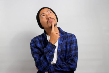 Şapka ve günlük gömlek giyen düşünceli genç Asyalı adam, elini çenesinde dinlendiriyor, boş fotokopi alanına bakıyor, derin düşünce ve gelecek için planlar yapıyor.