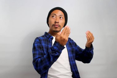 Şapka ve gündelik gömlek giymiş genç bir Asyalı ellerini dua etmek için tokalaşıyor, zarafet, umut, af diliyor, dini bir kavramı somutlaştırıyor. Beyaz bir arkaplanda izole edilmiş