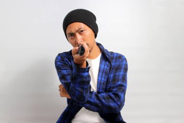 Sıkılmış genç Asyalı bir adam, bereli bir şapka ve günlük bir gömlek giyer, elinde uzaktan kumanda ile televizyon izlerken farklı kanallarda dolaşır, ilginç bir program arar, beyaz arka plan,