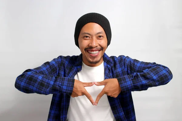 stock image Young Asian man, dressed in a casual shirt and wearing a beanie hat, is creating a triangle shape with his hands, symbolizing the concept of environmental protection, recycling, and reusing