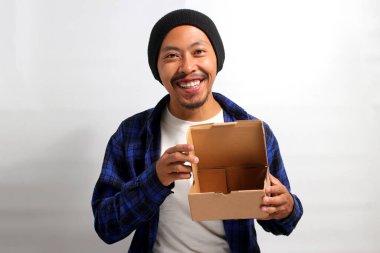 Şapka ve günlük gömlek giymiş neşeli bir Asyalı adam, beyaz bir arka fona karşı durarak kameraya açılmış bir karton kutuyu gururla sergiliyor.
