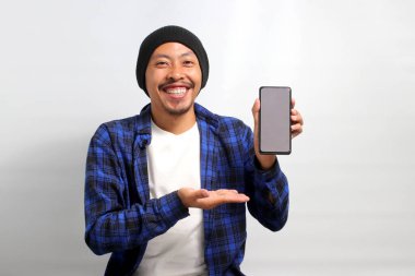Gülümseyen Asyalı adam beyaz arka planda dururken yeni bir uygulama ya da özel bir teklif önerirken kameraya cep telefonuyla boş bir beyaz ekran gösteriyor.