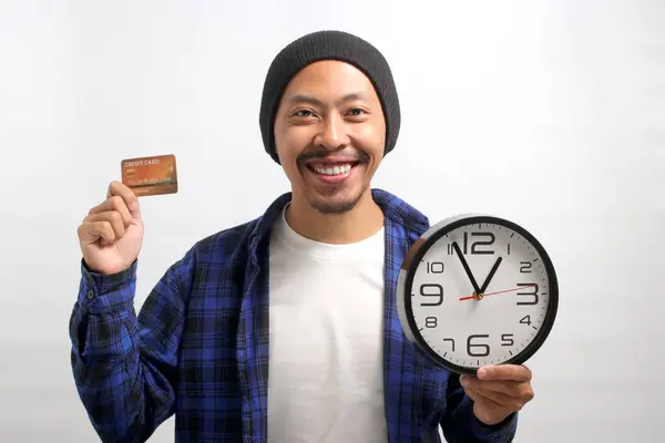An Asian man, dressed in a beanie hat and casual shirt, holds a clock and a credit card, signaling a limited time sale promotion while standing against a white background