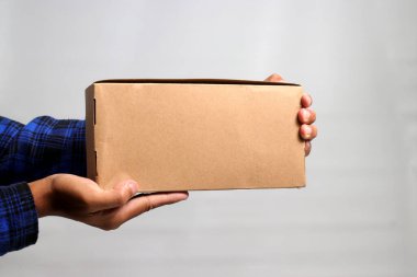 Gri bir arkaplana karşı karton kutu tutan bir el, nakliye, teslimat ve lojistik hizmetleri kavramını gösteren