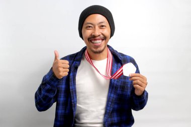 Bere şapkalı ve sıradan gömlekli heyecanlı bir Asyalı genç adam, beyaz bir arkaplanda tasvir edilmiş, madalyalar kazanırken gururla kameraya gülümseyen, bir işaret veriyor.