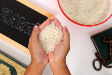 Hand holding a pile of rice for Zakat al-Fitr, with the Holy Quran, prayer beads or tasbih, and Zakat sign on a white background. Zakat Fitrah is a mandatory form of charity during Ramadan clipart