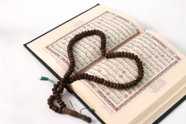 Kutsal Kur 'an' ın üzerine yerleştirilmiş, beyaz bir arka planda izole edilmiş sevgi ve sadakati ifade eden tespih ya da tasbih.
