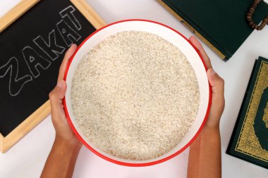 Hand holding a bowl of rice for Zakat al-Fitr, with the Holy Quran and Zakat sign on a white background. Zakat Fitrah is a mandatory form of charity given by Muslims during Ramadan clipart
