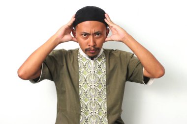 Koko gömlekli ve göğüs kaslı endişeli Endonezyalı müslüman panik ve endişe jesti ile başını tutuyor. Kameraya endişeli bir ifadeyle bakıyor, bir başarısızlık hissi veriyor. Beyaz arkaplan