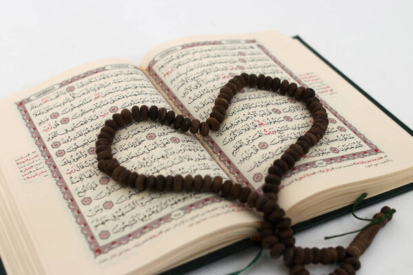 Prayer beads or Tasbih arranged in a heart shape on the Holy Quran, expressing love and devotion, isolated on a white background