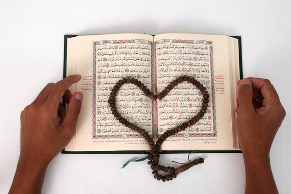 Prayer beads or Tasbih arranged in a heart shape on the Holy Quran, expressing love and devotion, isolated on a white background