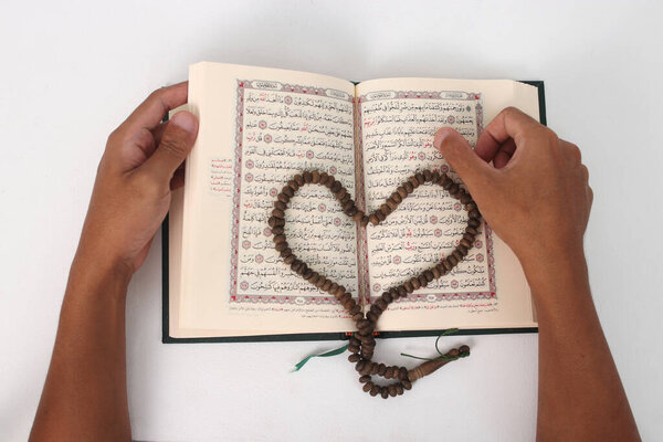 Prayer beads or Tasbih arranged in a heart shape on the Holy Quran, expressing love and devotion, isolated on a white background