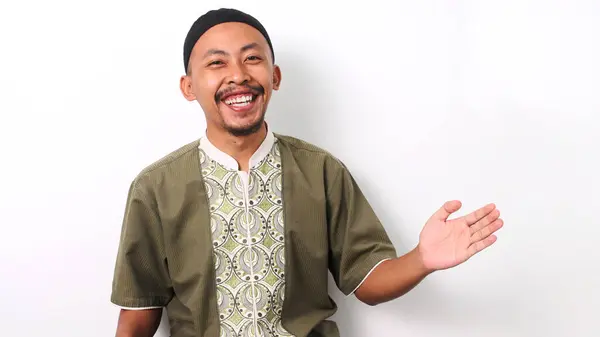 stock image Indonesian Muslim man in koko shirt and peci extends his arms wide in a welcoming gesture, leaving space for text or advertisement. Isolated on a white background