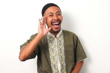 An Indonesian Muslim man in koko and peci cups his hand near his mouth in a gesture of announcement or sharing information. Isolated on a white background clipart