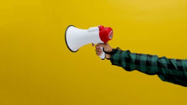 El ele tutuşan bir megafon, sarı arka planda izole edilmiş.