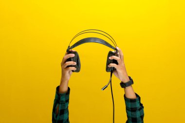 Siyah bir kulaklığı parlak sarı bir arka plana doğru tutuyor. Müzik, ses ekipmanı veya ses teknolojisi gibi kavramları resmetmek için idealdir..