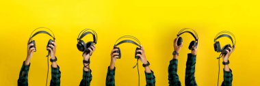 Siyah bir kulaklığı parlak sarı bir arka plana doğru tutuyor. Müzik, ses ekipmanı veya ses teknolojisi gibi kavramları resmetmek için idealdir..