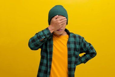 Utangaç genç Asyalı bir adam, bereli bir şapka ve günlük bir gömlek giyer, bir hata fark ettikten sonra tedirgin, sıkıntılı, bitkin ve pişmanlık dolu bir yüz ifadesi sergiler.