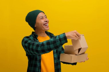 Mutlu Asyalı müşteri karton kutuyu açarken gülümsüyor, yukarıdaki boş kopya alanına bakıyor, sarı arkaplanda izole edilmiş..