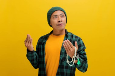 Şapka ve gündelik gömlek giymiş genç bir Asyalı ellerini dua etmek için tokalaşıyor, zarafet, umut, af diliyor, dini bir kavramı somutlaştırıyor. Sarı arkaplanda izole edilmiş