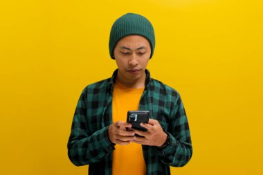 Mutlu ve şaşkın Asyalı adam, beresi ve günlük gömleği olan, akıllı telefonunu mesajlaşma, sosyal medya sözleşmesi, online ekommerce alışverişi, mobil uygulamalar veya video izlemek için kullanıyor