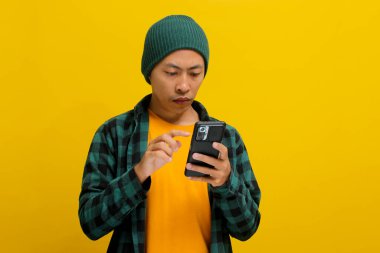 Mutlu ve şaşkın Asyalı adam, beresi ve günlük gömleği olan, akıllı telefonunu mesajlaşma, sosyal medya sözleşmesi, online ekommerce alışverişi, mobil uygulamalar veya video izlemek için kullanıyor